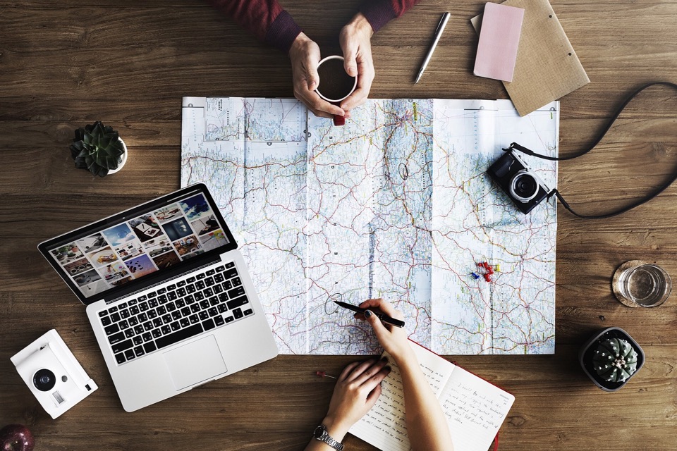 Two travellers reviewing a paper map beside a laptop and coffee